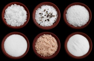 six terracotta plates with different salt - flakes sea salt, coarse sea salt with crashed black pepper, coarse sea salt, fine sea salt, smoked flaky sea salt, table salt, Isolated on black