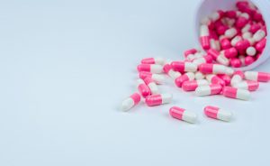 Pink-white capsule pills spread out of drug bottle. Antipsychotic drug. Capsule medicine for treatment depression. Anti-anxiety drug. Global healthcare. Pharmacy background. Pharmaceutical industry.