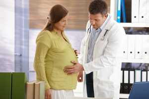 Doctor touching pregnant woman's belly in consuting room.