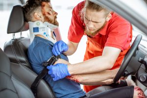 Medic wearing tourniquet on arm of injured person sitting on the driver saet after the road accident, providing emergency medical assistance