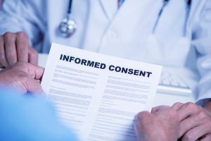 closeup of a senior caucasian man, at the doctors office, reading an informed consent document in front of a caucasian doctor man, in a white coat, sitting both at the doctors desk