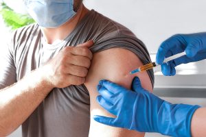 Hands of doctor injecting coronavirus covid-19 vaccine in vaccine syringe to arm muscle of caucasian man for covid immunization. Bearded man wearing protective mask getting ready to be vaccinated.