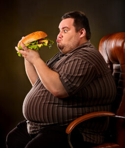 Diet failure of fat man eating fast food hamberger. Happy smile overweight person who spoiled healthy food by eating huge hamburger on fork. Obesity due to eating bad foods. Very fat man eating fast