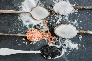 Different Kinds of Salts in Spoons such as Himalayan Pink Salt Sea Salt Original Iodised Table Salt Sea Salt Flakes Pink Salt Diamonds Black Sea Salt Flakes on Dark Background