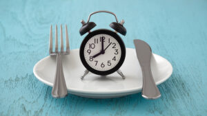 Clock on notepad with fork and knife, intermittent fasting and weight loss plan concept